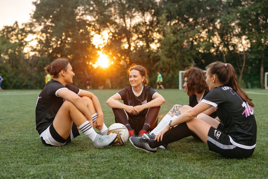 A group of female soccer players sitting on a field, celebrating after a match at sunset.